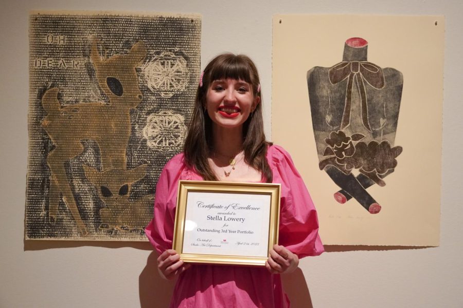 Stella standing in front of two of her pieces holding the Third-Year award plaque.