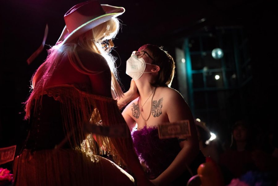 Sancho Stardust caresses a fan who stands in the audience beside the stage while dollar bills fall through the air.