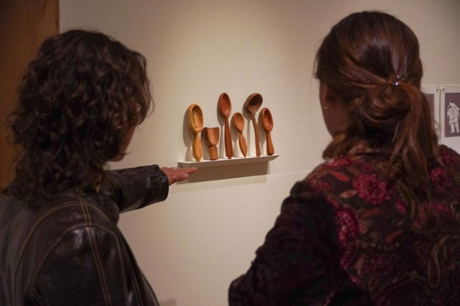 Two gallery attendees stand looking at Kelly Banfields piece Sisterhood of the Traveling Spoons.
