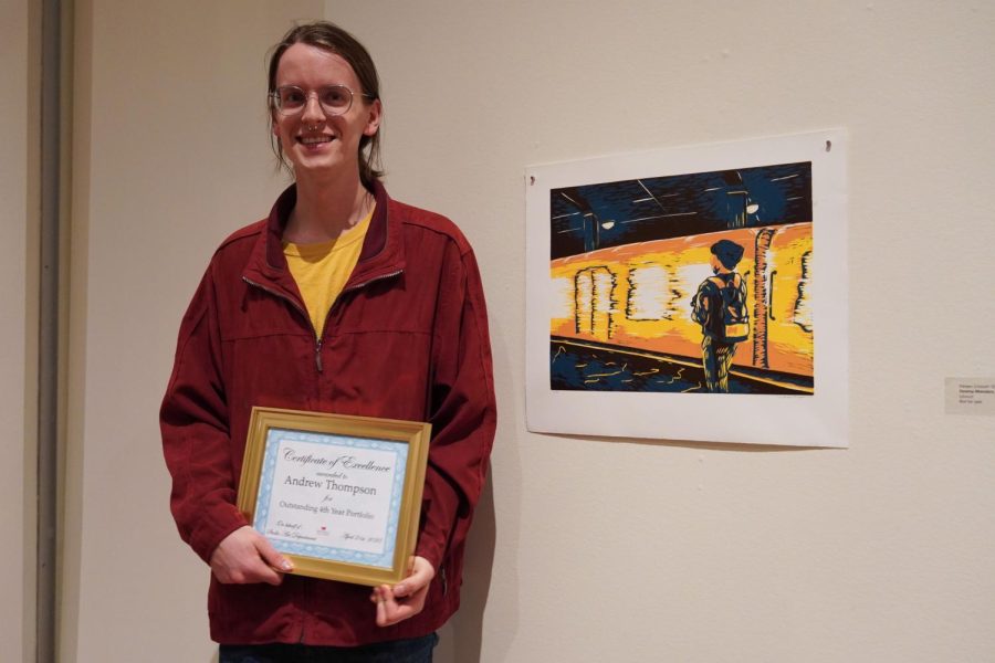 Andrew standing in front of one of his prints holding his award plaque.