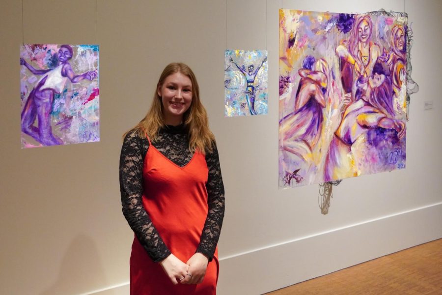 Celia standing between three of her paintings suspended by string from the ceiling.