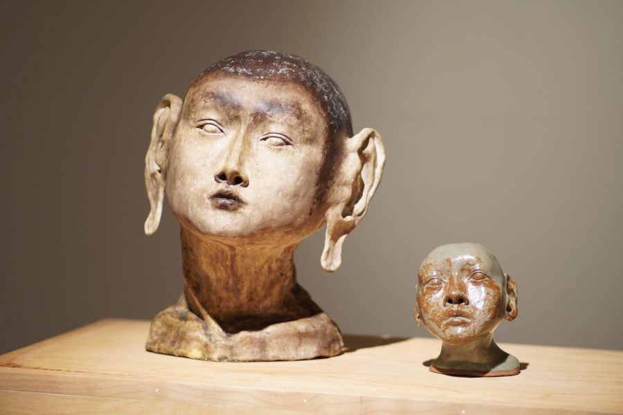 Two clay heads from the shoulders up, one with long earlobes and the other only a third the size with an inquisitive look.