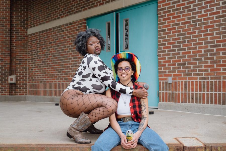 Cosmic Cunt Quixote poses in a cow-print body suit and fishnet stockings next to Cosmic Cunt Wrangler who sits in a rainbow cowboy hat, red flannel and jeans.