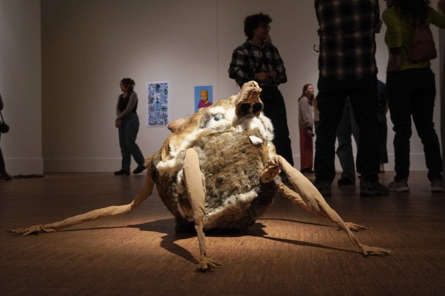 A round sculpture rests on the gallery floor covered in rabbit pelts with two arms and two legs splayed.
