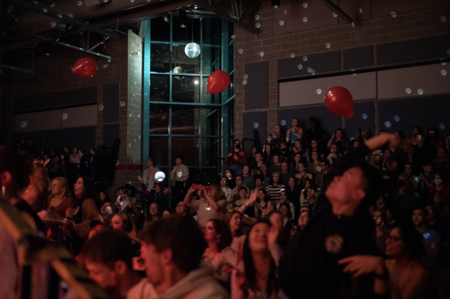 Crowd members dance and reach for the balloons falling through the air as light refracts from the spinning disco ball above.