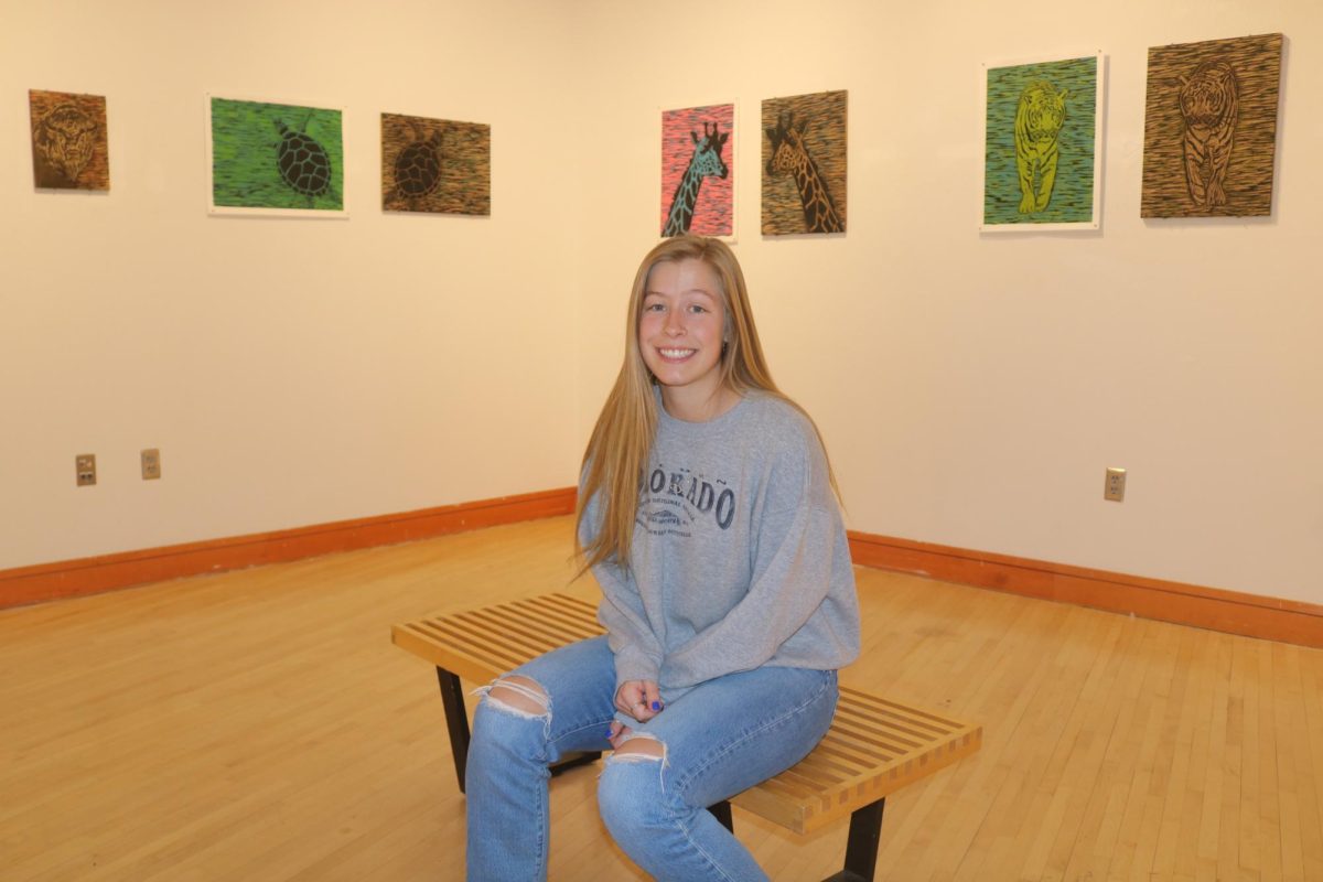 Kathryn Vermeulen `24 sits in the center of Smith Gallery, her art adorning the walls behind her. She enlisted a friend to help her set up the exhibition in time.