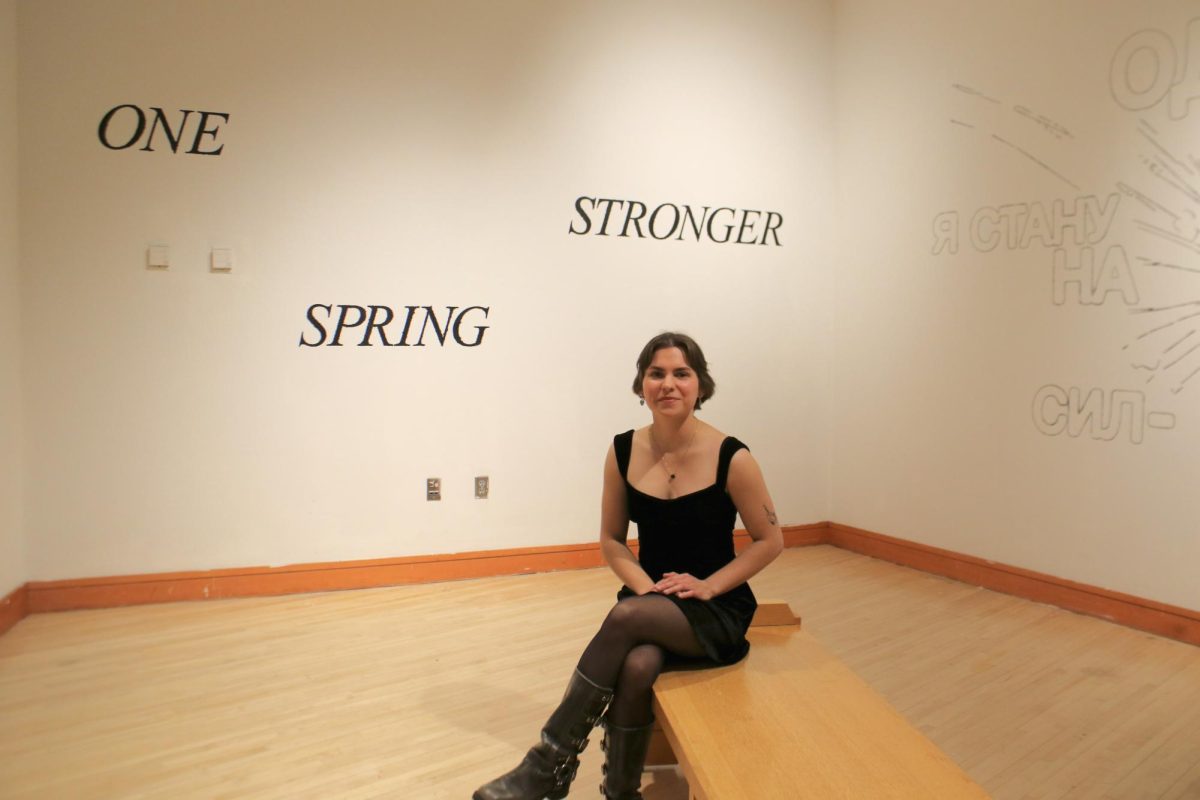 Alina Ihnatesku `26 sits in her gallery exhibition amidst walls that say ONE STRONGER SPRING in English and Russian, respectively.