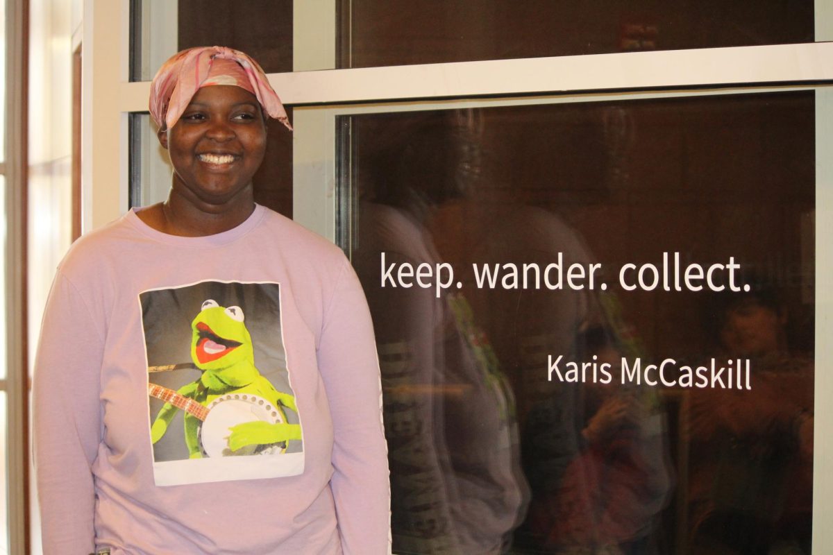 Karis McCaskill `24 grins in front of the gallery wearing a Kermit sweater — a green frog to match the green leaves in her exhibition.