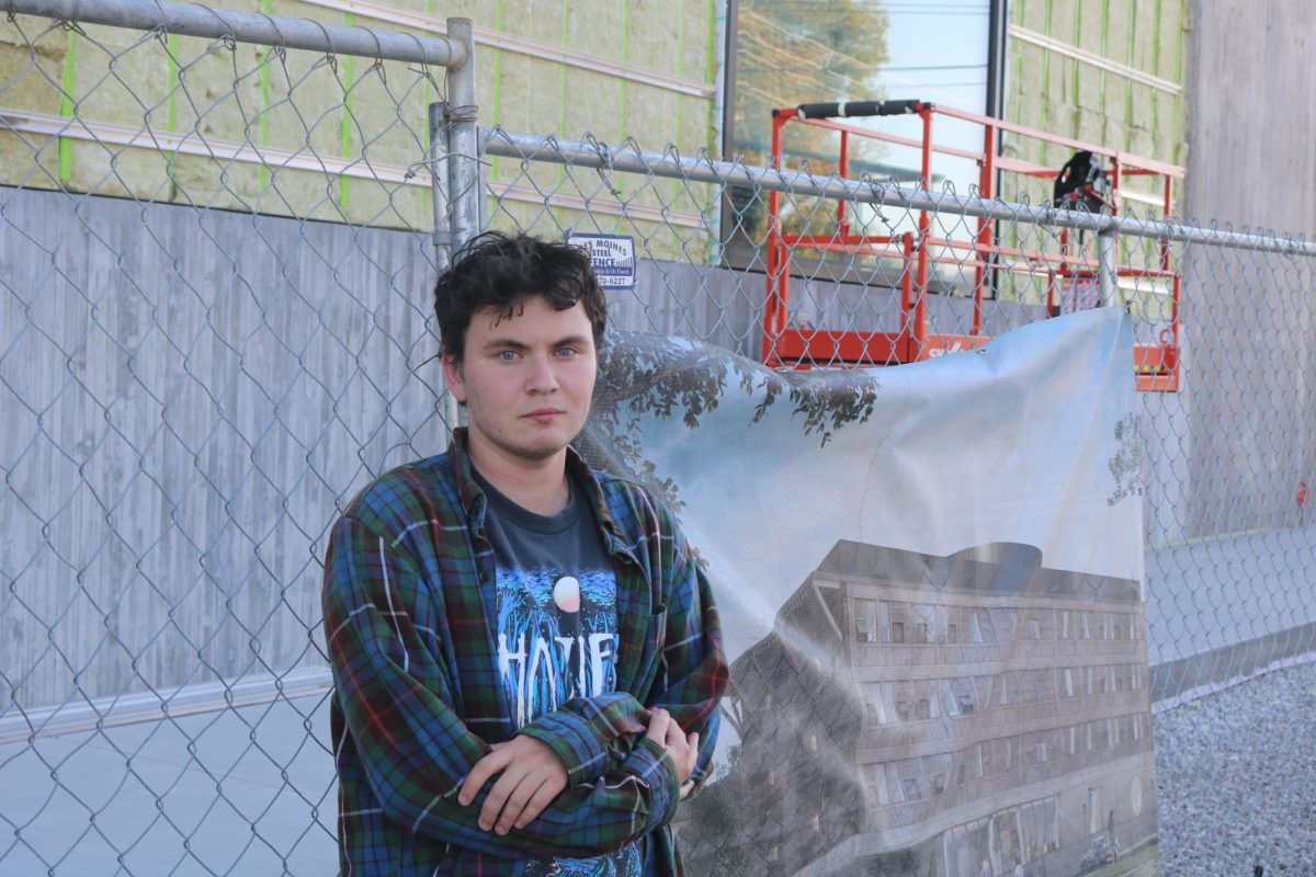 Victor Thorne `26 poses in front of the Renfrow Hall construction site, where a mock-up of the finished building hangs on the chainlink fence behind him.