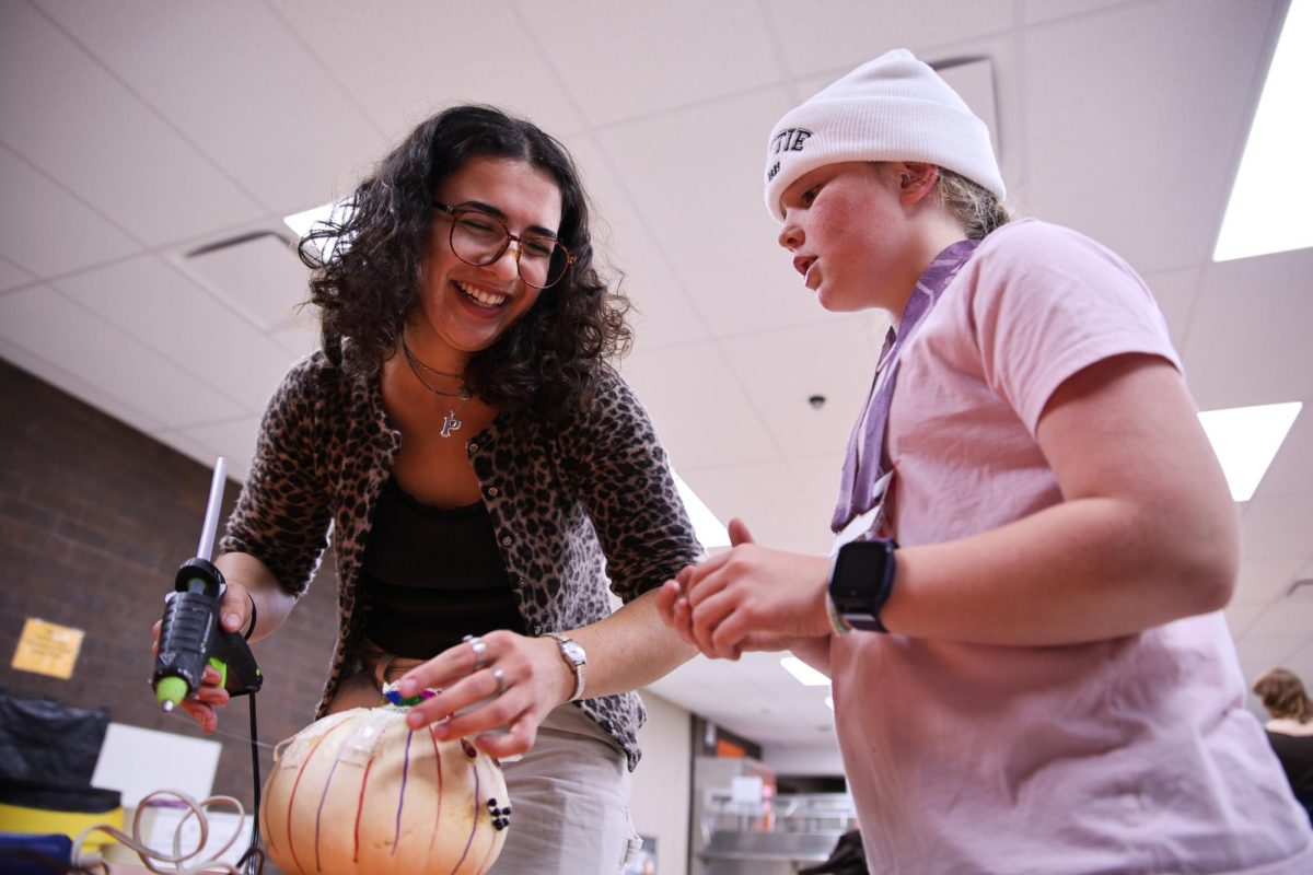 From left: Philomena Frasca `25 laughs with Mari Hurst, 10, as they decorate a pumpkin at Grinnell Middle School on Nov. 1, 2024.