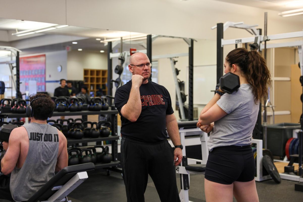 Coach Steve Lewis shows tennis player, Isa Voinescu '26, proper form during a team lift in the Bear Fitness Center.