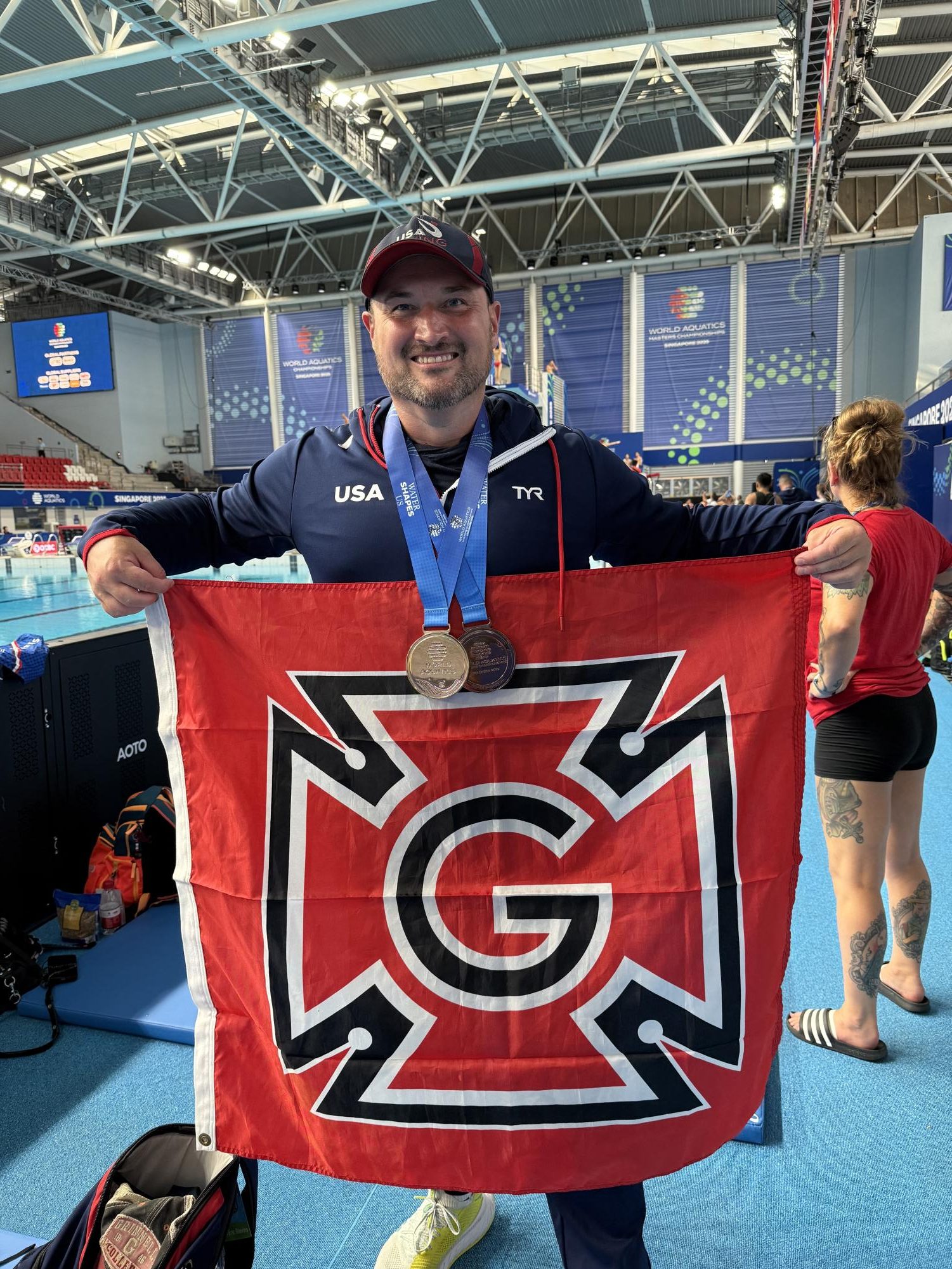 Eric Blevins `04 poses with his Honor G flag and two medals at the World
Aquatics Masters Championships in Singapore. Contributed by Eric Blevins.
