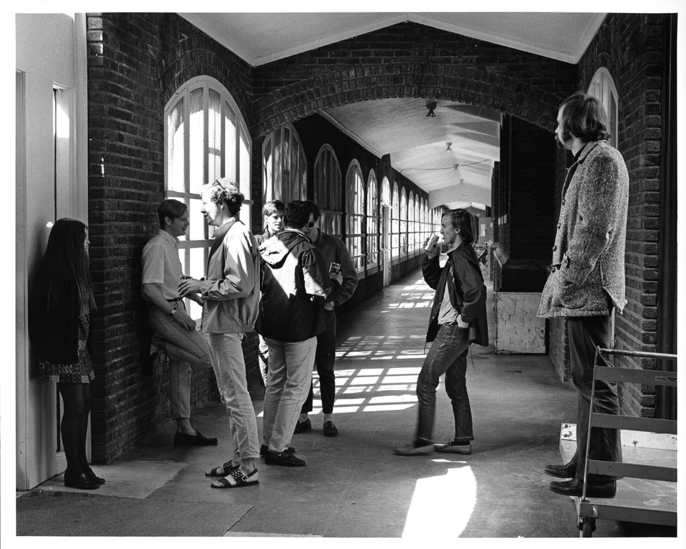 Students gather in South Campus loggia, notably there is only one female student and seven male students. 