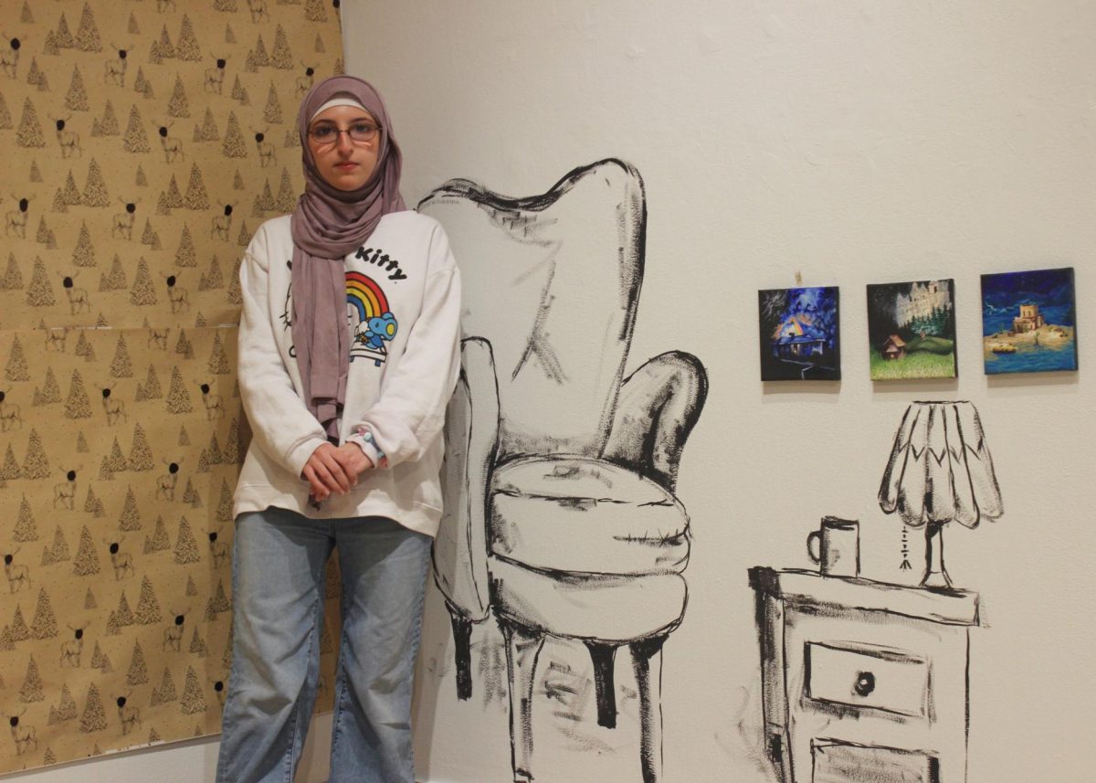 A’ishah Mokrani `27 poses in front of the chair and stool she drew onto the white walls of the Edith Renfrow Smith `37 Gallery.