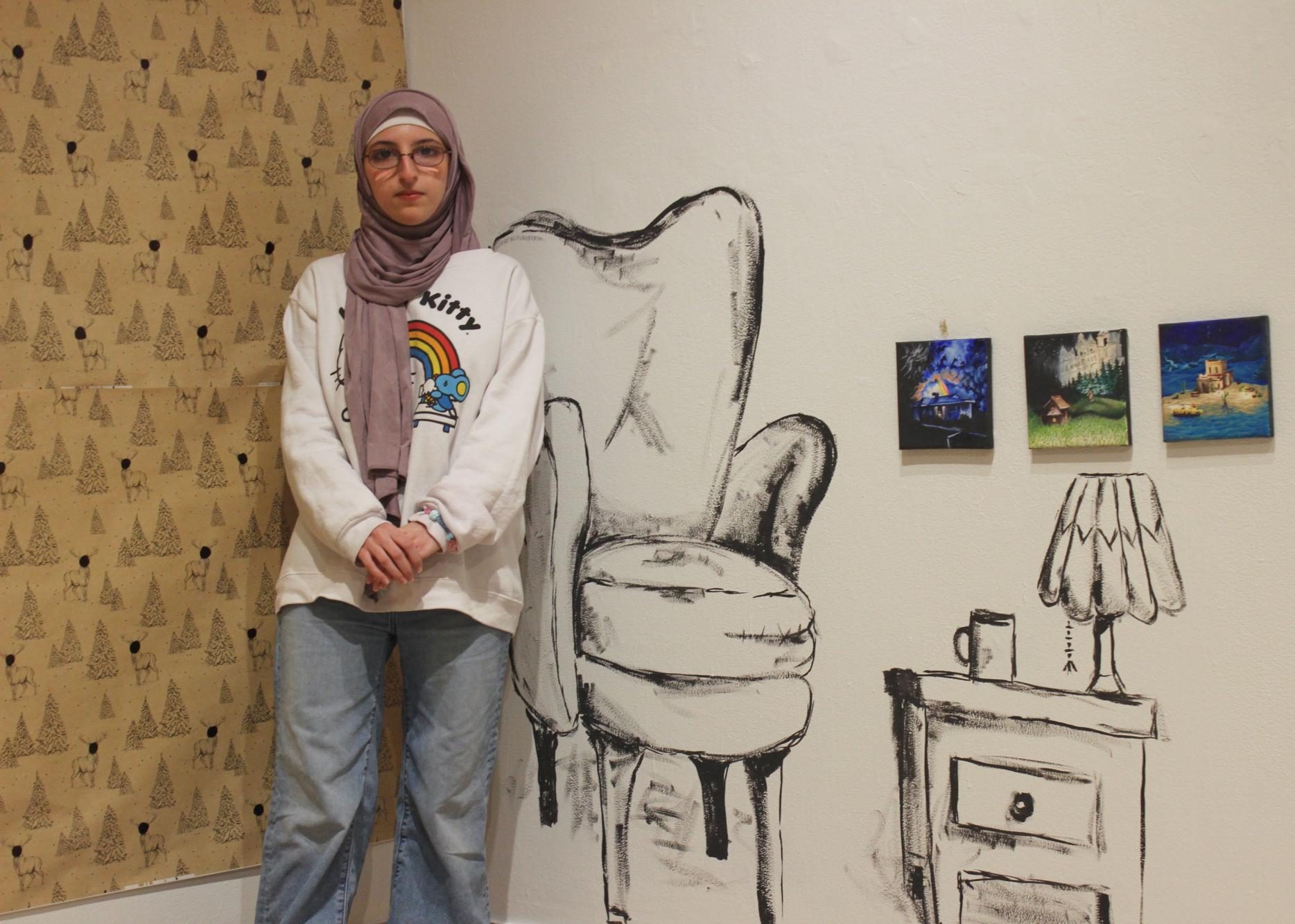 A’ishah Mokrani `27 poses in front of the chair and stool she drew onto the white walls of the Edith Renfrow Smith `37 Gallery.