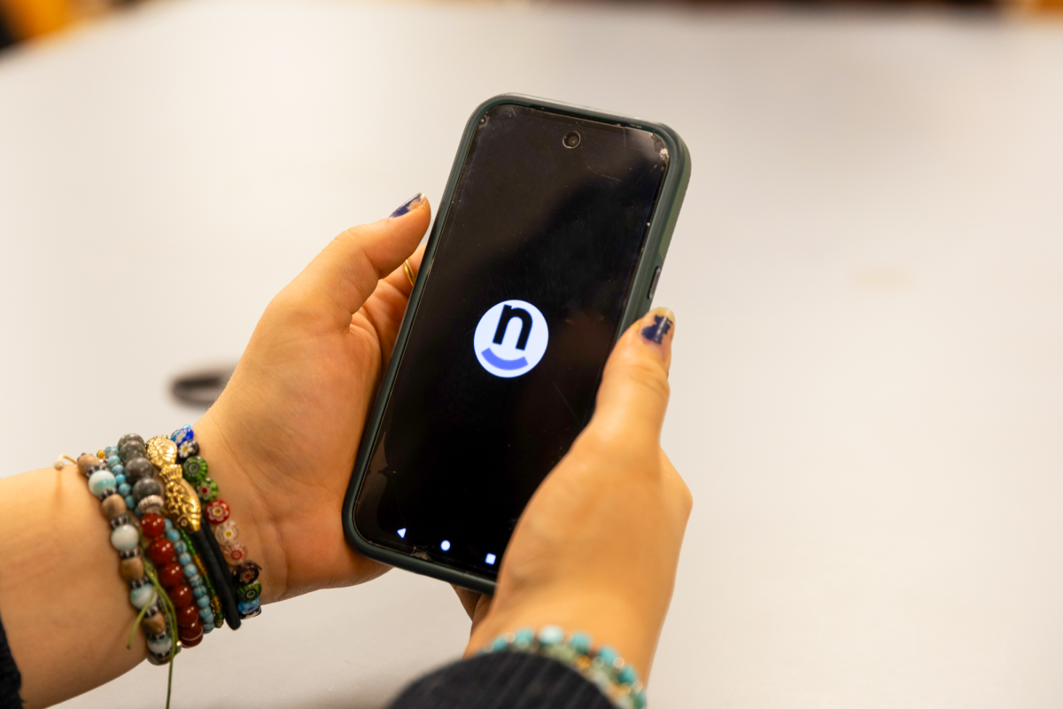 Natalie Sato `27 poses with the Nutrislice app on her phone to check lunch options at the dining hall on Tuesday, Feb. 3.