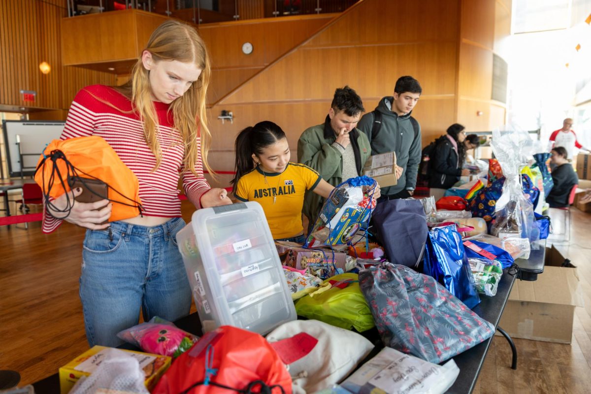 From left: Faye Henn `26, Hikaru Aoki `26 and Victor Thorne `26 look through the alumni care packages in JRC 101 on Tuesday, Feb. 24.